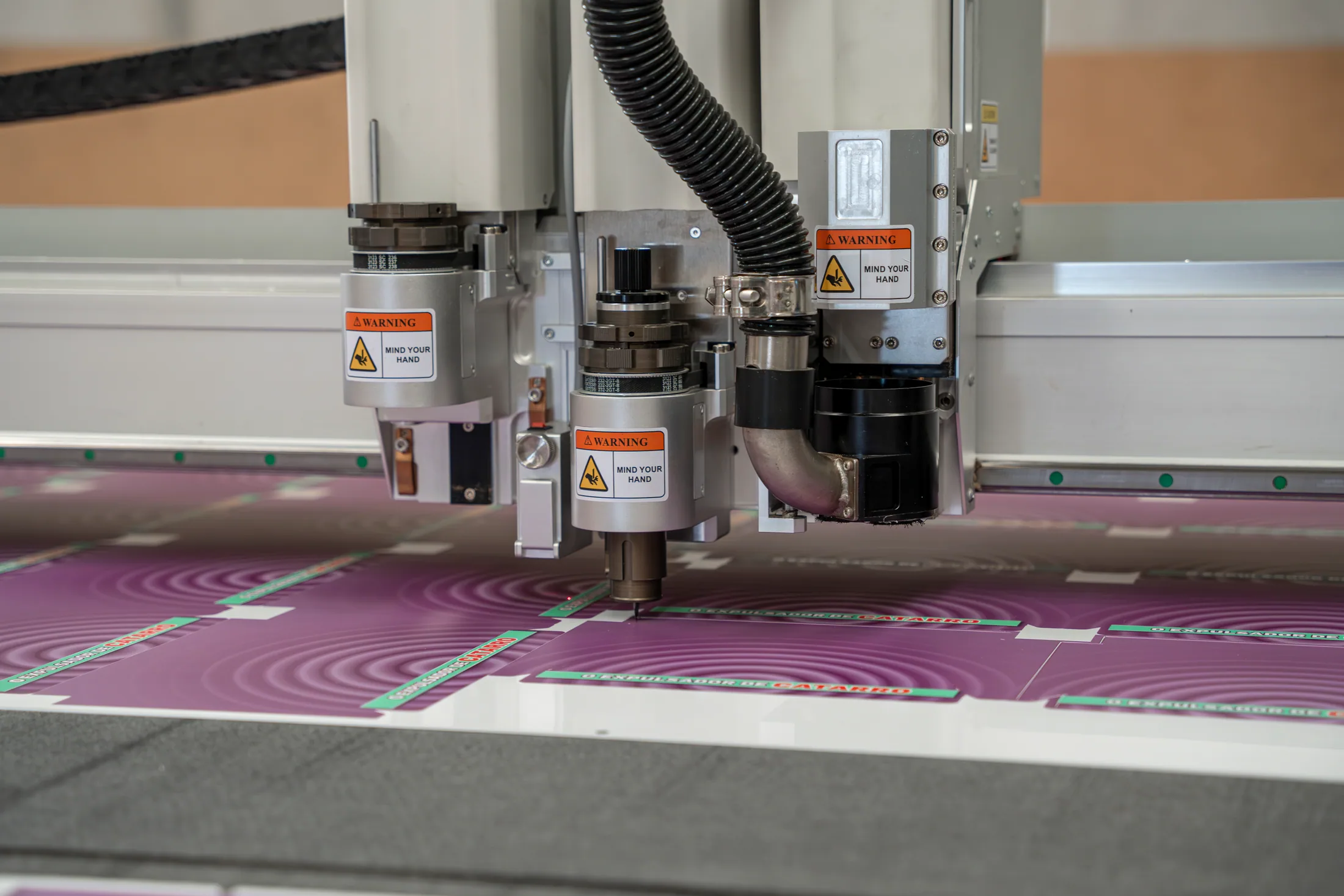 Detalhe aproximado das ferramentas de uma mesa de corte digital cortando material impresso em magenta
