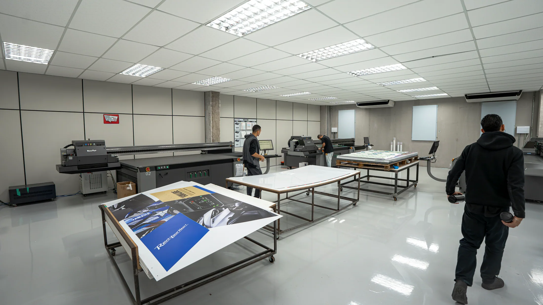 Vista ampla do showroom com impressoras de grande formato, mesas de apoio e peças impressas prontas para avaliação