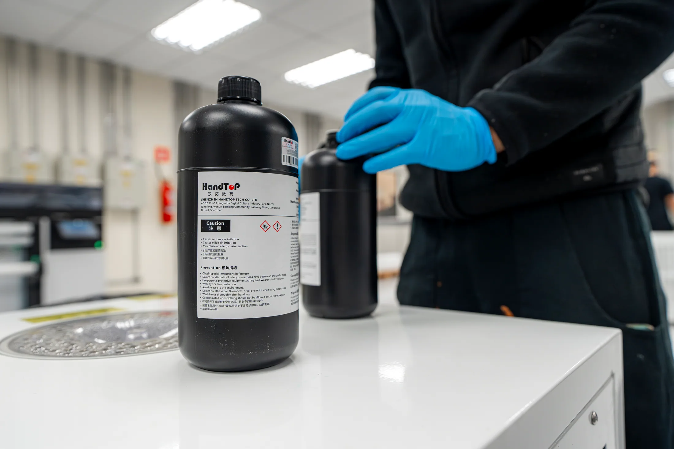 Frasco de tinta UV HandTop sobre a bancada, manuseado por um técnico de luvas